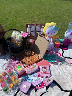 a picnic blanket with hello kitty food and drinks on it in the grass next to an open suitcase