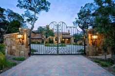 a gated driveway leading to a house with stone walls and iron gates that lead into the front yard