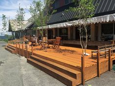 a large wooden deck with chairs and trees on the other side, in front of a building