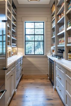 a kitchen with white cabinets and wooden flooring next to an open window that looks out onto the woods