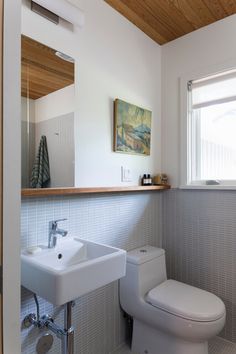 a white toilet sitting next to a bathroom sink under a window in a room with wooden ceiling