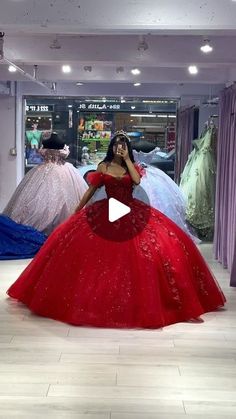 a woman in a red ball gown standing in front of dresses on mannequins