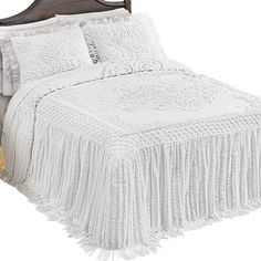 a white bed with fringed bedspread and pillows