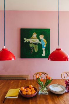 a painting hangs above a dining room table with oranges and bowls on the table