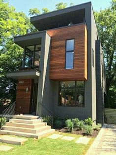 a modern house with wood siding and stairs leading up to the second floor, in front of some trees