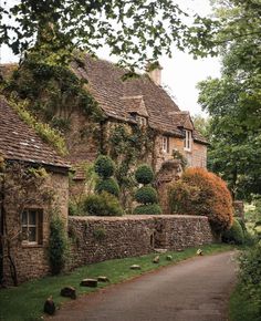 an old stone house is surrounded by greenery and trees on either side of the road