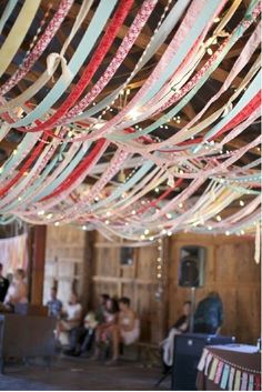 many ribbons are hanging from the ceiling in a room with people sitting and standing around