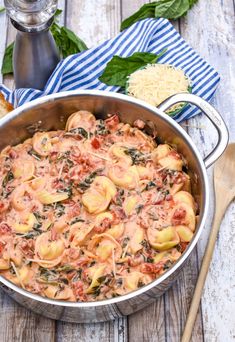 a pot filled with pasta and sauce on top of a wooden table next to bread