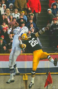 two football players jumping in the air to catch a ball while people watch from the bleachers