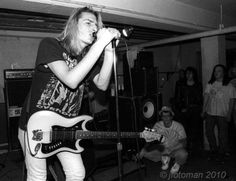 a woman singing into a microphone while holding a guitar in front of her and other people watching