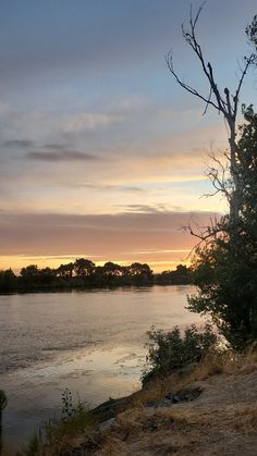 the sun is setting over the water and trees