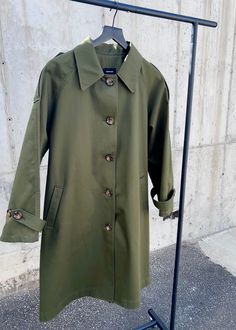 an army green coat hanging on a clothes rack in front of a concrete wall,