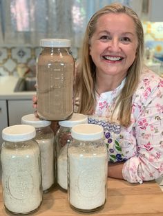 a woman is holding up some jars on a table