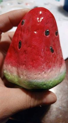 a hand holding a watermelon slice in it's left hand, with black dots on the top