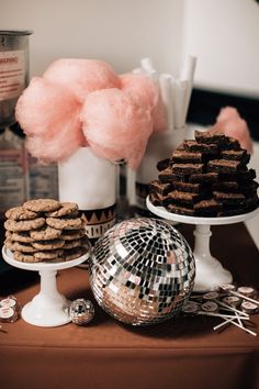 a table topped with cakes and cookies next to a vase filled with pink fluffy balls