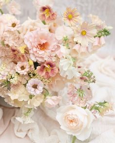 a bouquet of flowers sitting on top of a white cloth covered tablecloth next to a vase filled with pink and yellow flowers