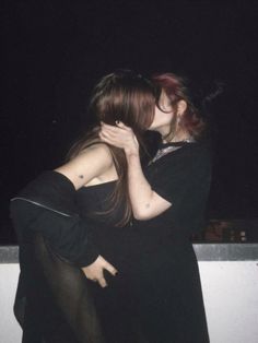 two people are hugging each other on the roof at night time, one is wearing black and the other has red hair