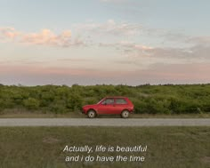 a red car parked on the side of a road next to a lush green field