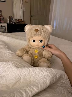 a person holding a teddy bear on top of a bed with white sheets and pillows