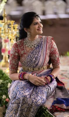 a woman sitting on the ground wearing a blue and white sari with gold jewelry