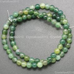 two strands of green and white beads with silver clasps on a gray table top