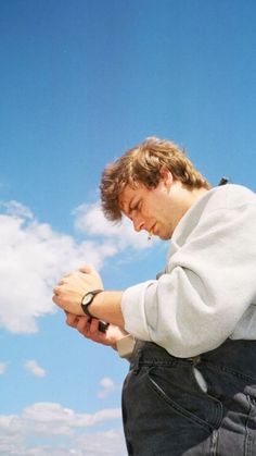 a young man holding onto his watch while standing in front of a blue sky with clouds