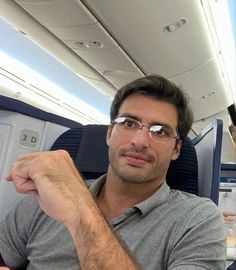 a man sitting on an airplane with his arm crossed and looking at the camera while wearing glasses