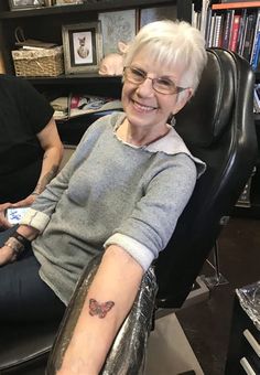 an older woman sitting in a chair with a tattoo on her arm