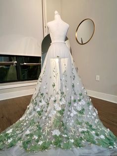 a white dress with green and white flowers is on display in front of a mirror