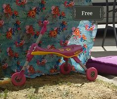 a child's tricycle sitting on the ground next to a flowered blanket