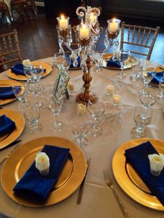 the table is set with gold plates and blue napkins, silverware, and candles