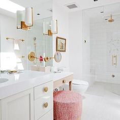 a white bathroom with gold accents and pink stool