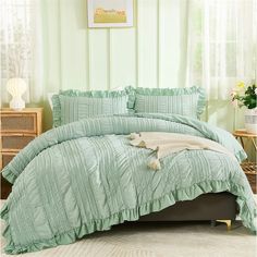 a bed with green comforter and pillows on it in front of a white wall