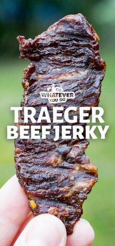 a hand holding up a piece of beef with the words tracer beef jerk on it