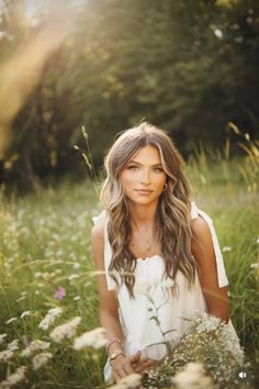 a beautiful young woman sitting in the middle of a field with wildflowers and grass