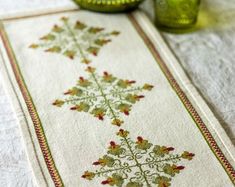 a white table runner with red and green designs on it next to two green vases