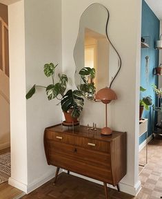 a mirror and some plants on a dresser in a room with blue walls, wood floors and wooden flooring