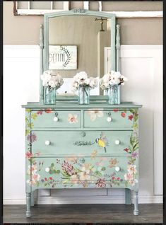 an old dresser with flowers painted on it and a mirror above the drawers is shown