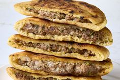 a stack of food sitting on top of a white plate next to a pile of meat patties