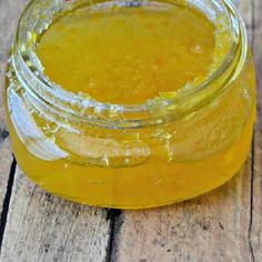 a jar filled with pineapple jam sitting on top of a wooden table next to an apple