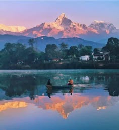 two people in a small boat on a lake with mountains in the background at sunset