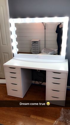 a white vanity with lights on it and a person standing in the mirror behind it