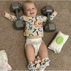 a baby laying on the floor with two dumbbells