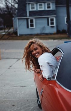 a woman leaning out the window of a red car