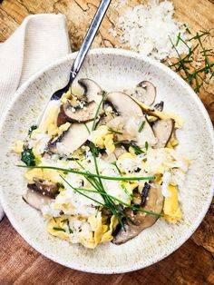 a white bowl filled with pasta and mushrooms on top of a wooden table next to rice