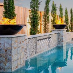 an outdoor fire pit next to a swimming pool with water running from it and plants growing on the wall