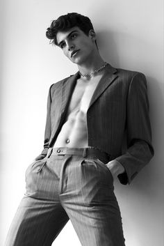 a man in a suit leaning against a wall with his shirt open and no shirt on