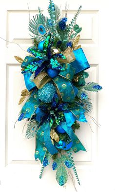 a blue and gold christmas wreath hanging on a white door with green feathers, pineconi and bells