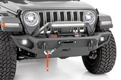 the front end of a gray jeep with its lights on and bumper mounted to it