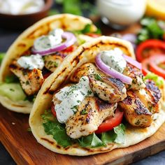 two tacos with chicken, lettuce and tomatoes on them sitting on a cutting board